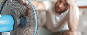 Young bearded man using electric fan at home